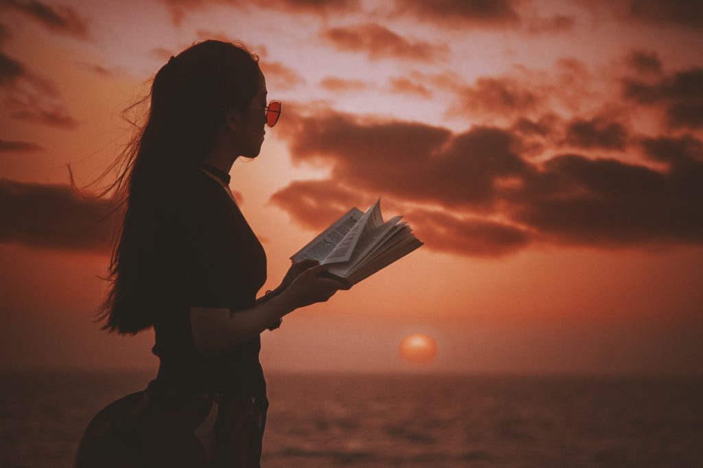 Woman reading book on beach at sunset.